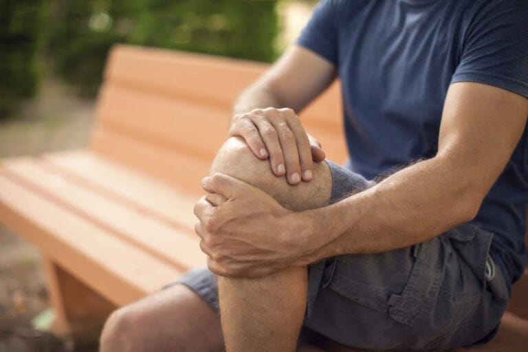 Man som masserar sitt knä sittande på en parkbänk