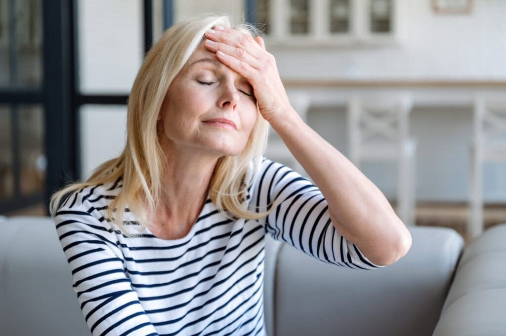 Kvinna sitter och håller sig för huvudet i smärta vid migrän.