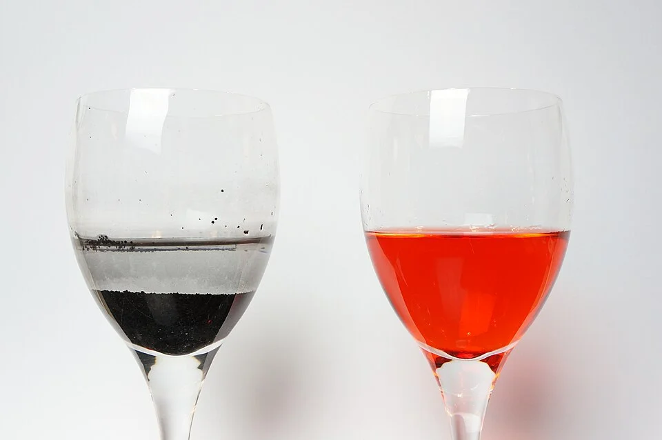 Två glas där aktivt kol i det vänstra har tagit upp det röda färgämne som finns kvar i det högra
